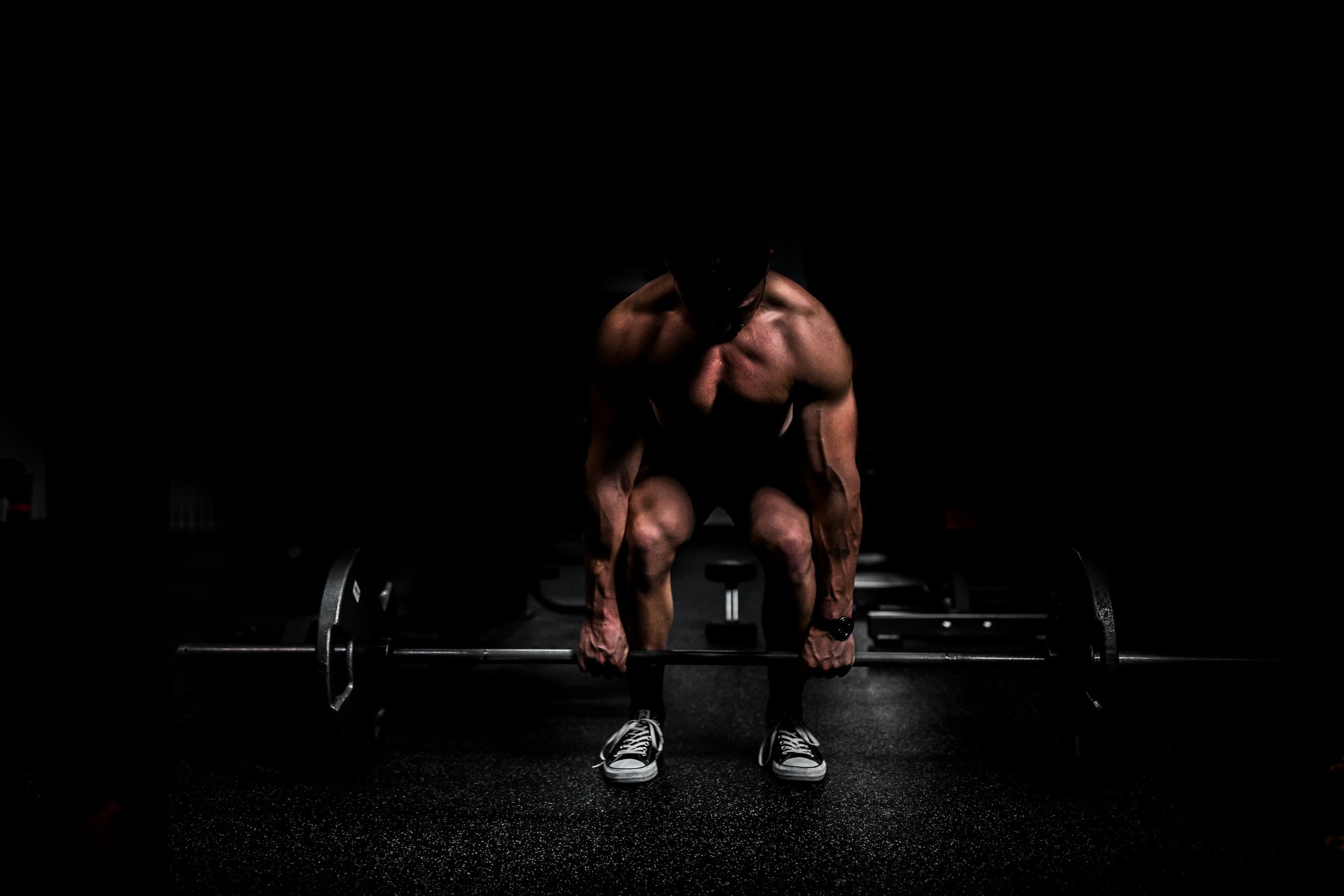 Anonymous athlete in low-key lighting bracing over a loaded barbell before a lift